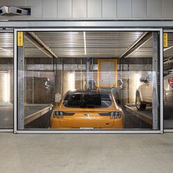 Obraz przedstawia żółty samochód sportowy w systemie parkingowym wewnątrz nowoczesnego garażu podziemnego.