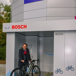 A man stands with his bicycle in front of the entrance to an automated bicycle parking tower