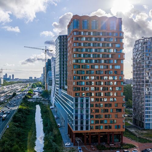 Widok zewnętrzny projektu The Pulse w Amsterdamie z nowoczesnymi wieżowcami oraz miejską infrastrukturą transportową.