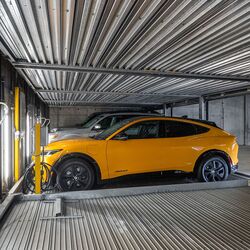 The image shows a car on a platform inside an automated parking system in a modern underground garage.